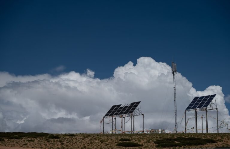 Solar panels and communication tower under a cloudy sky.