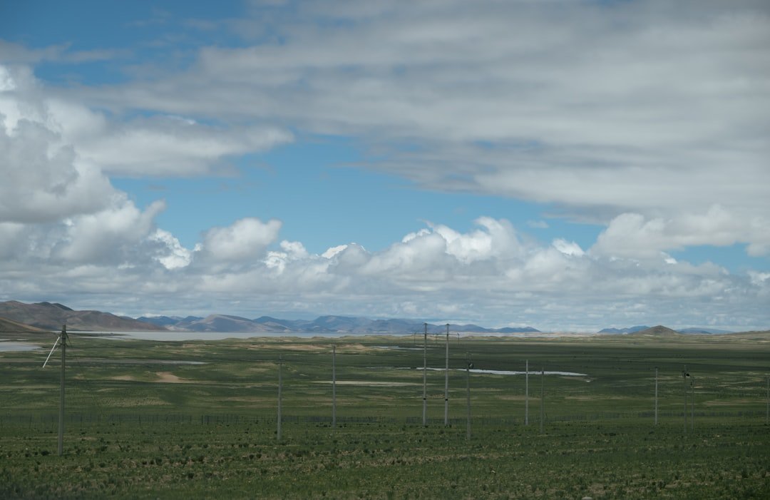 Expansive green field under a cloudy blue sky.