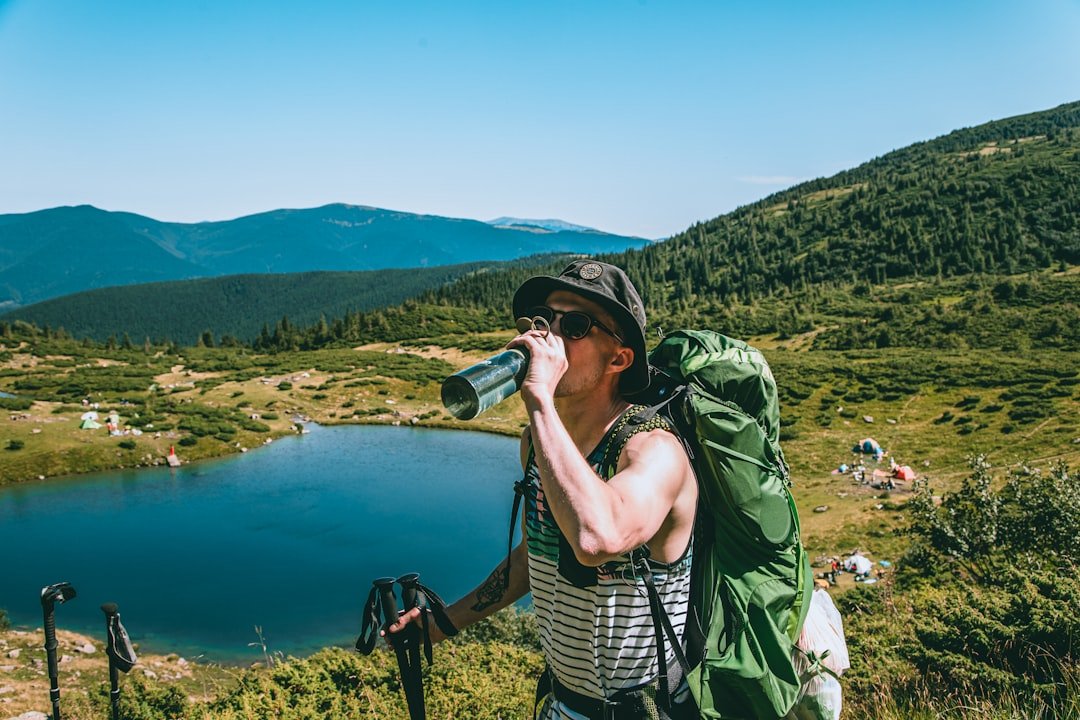 A man with a backpack drinking from a water bottle