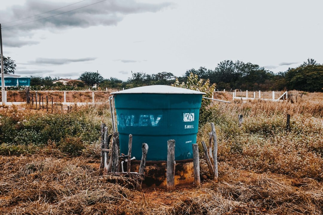 A teal water tank sits in a dry, grassy field.