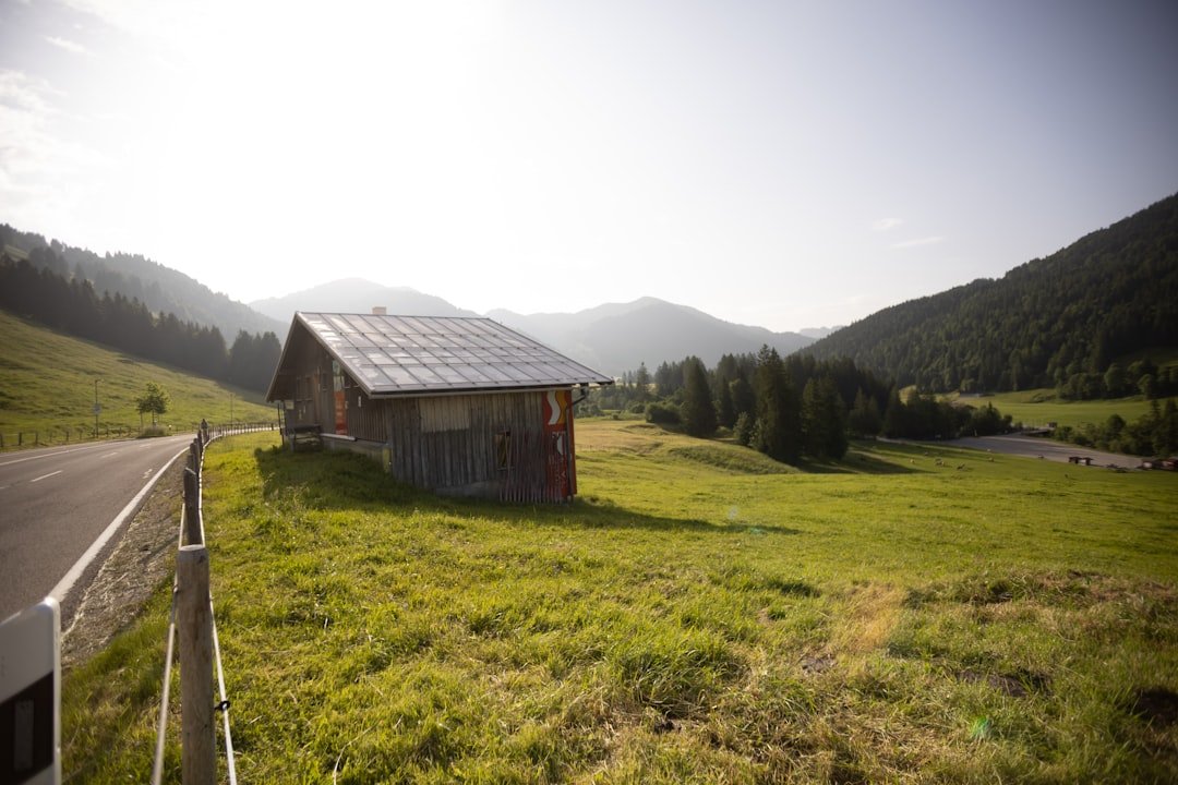 A cabin sits on a grassy landscape near mountains.