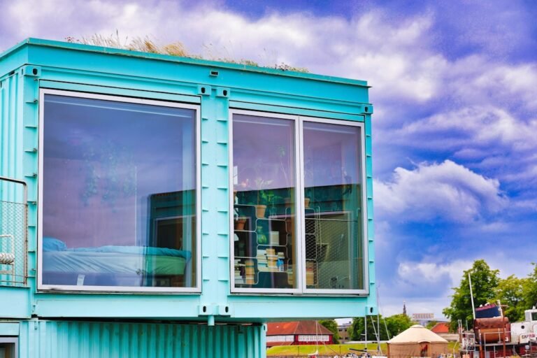 Modern turquoise shipping container home with large windows.